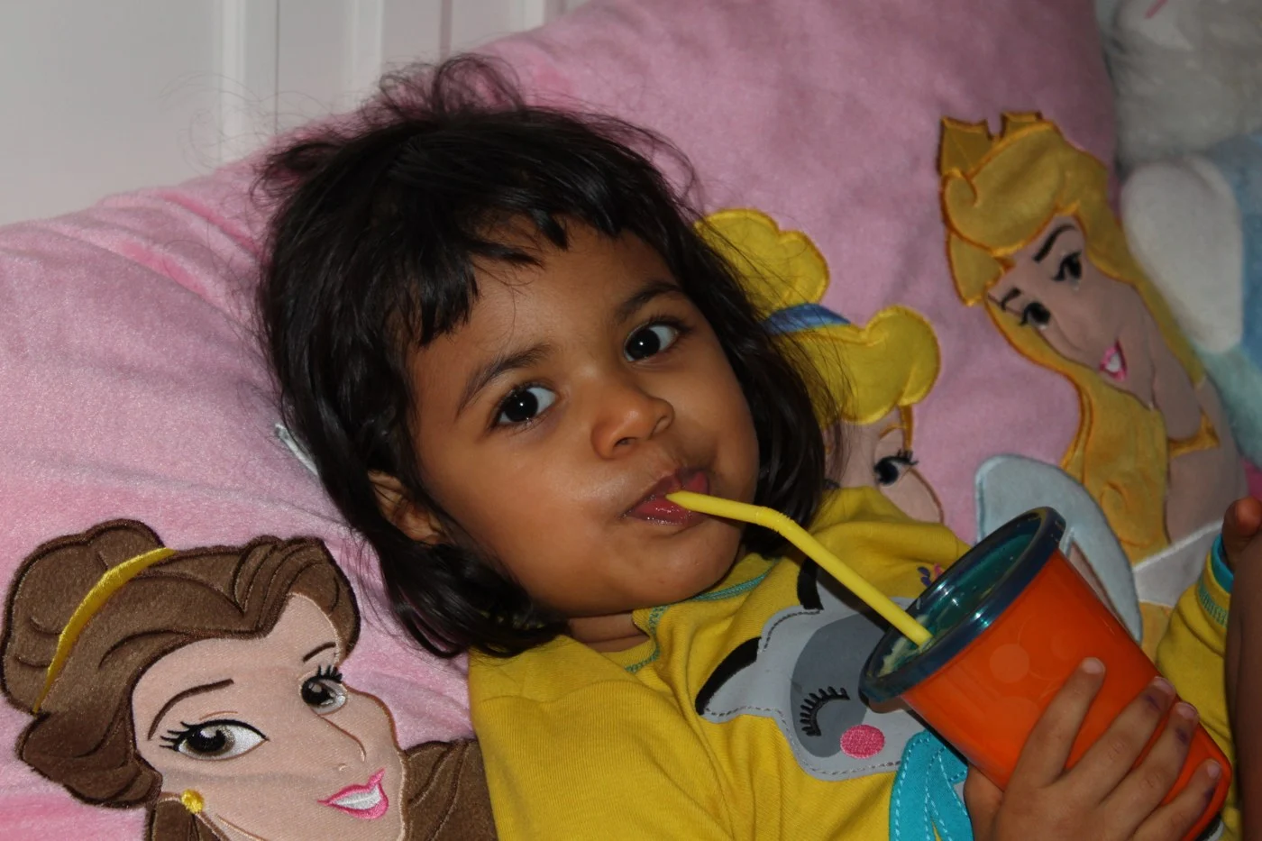 A child relaxing with an orange lidded cup and straw.
