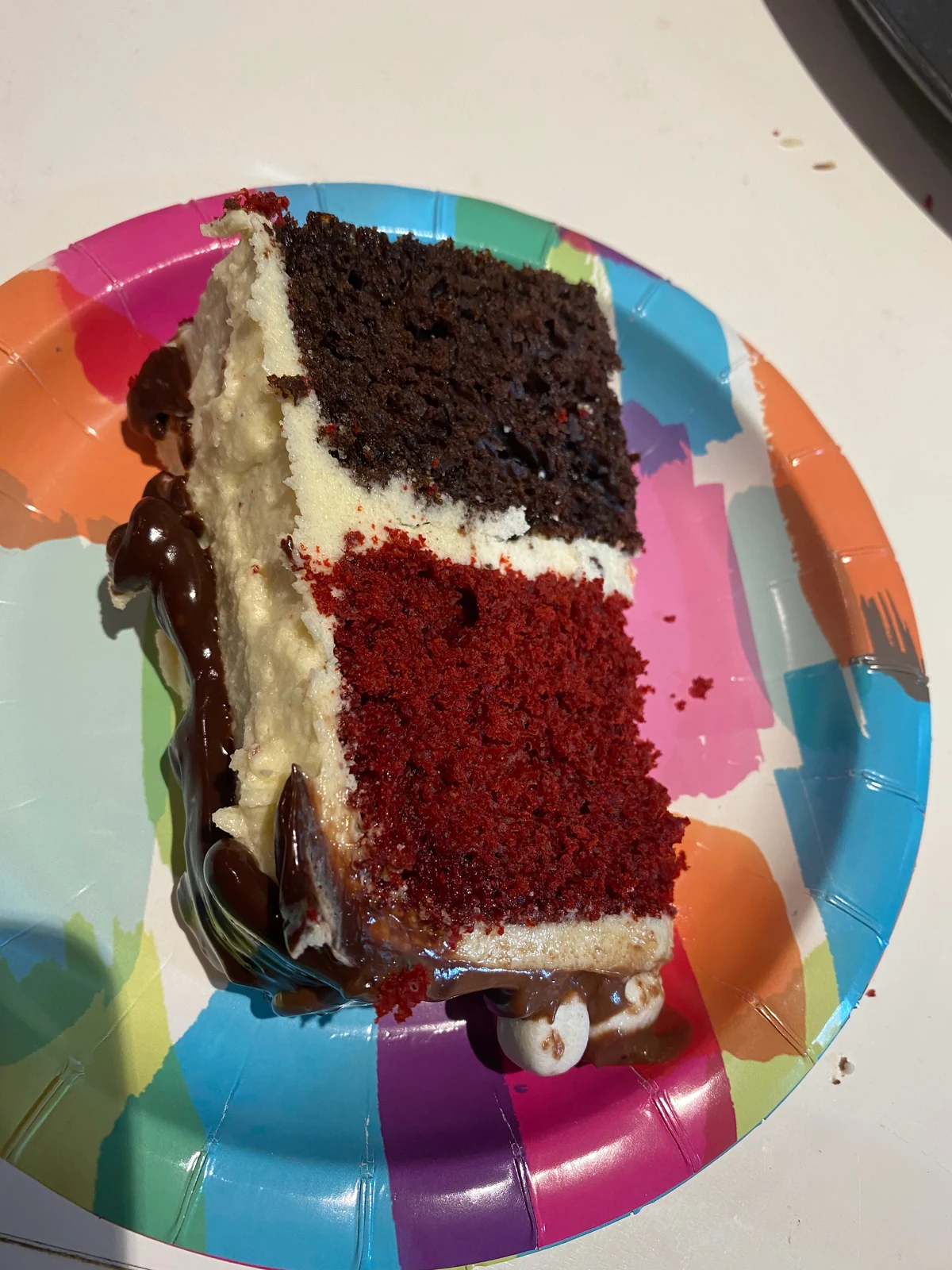 A slice of cake lying on its side, showing red and chocolate-colored crumb with pale frosting and ganache.