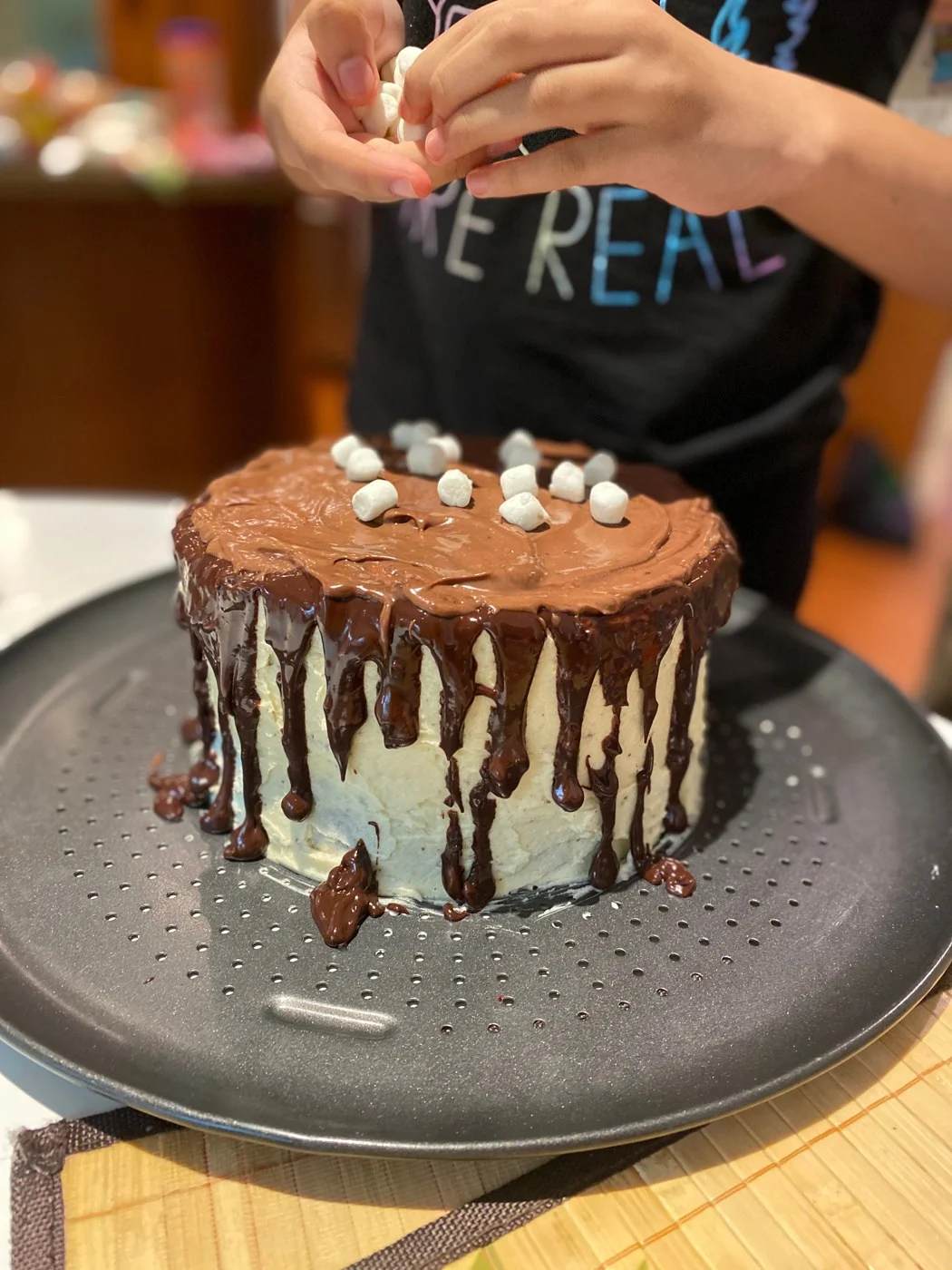 A baker decorating a drip cake with white marshmallows.