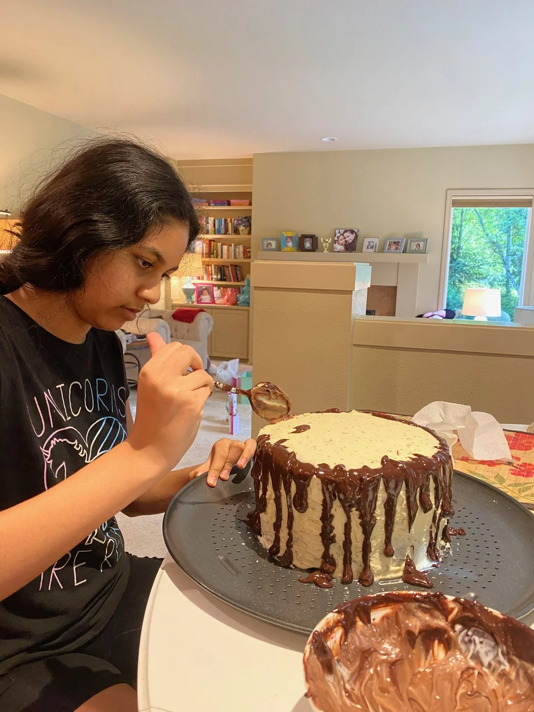 Applying chocolate drips around a round cake at the dining table.