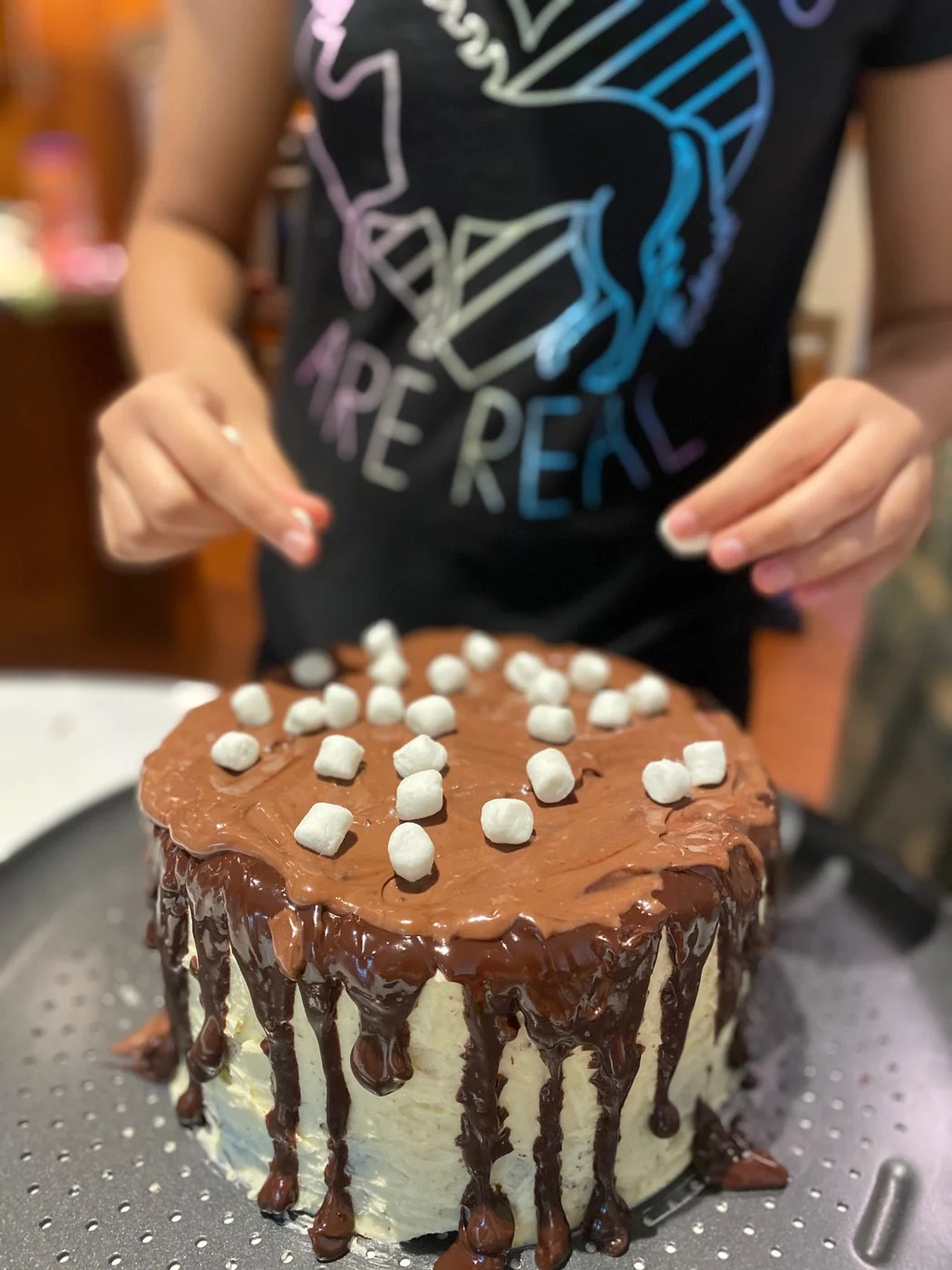 Placing the final white marshmallows across a chocolate-covered cake top.