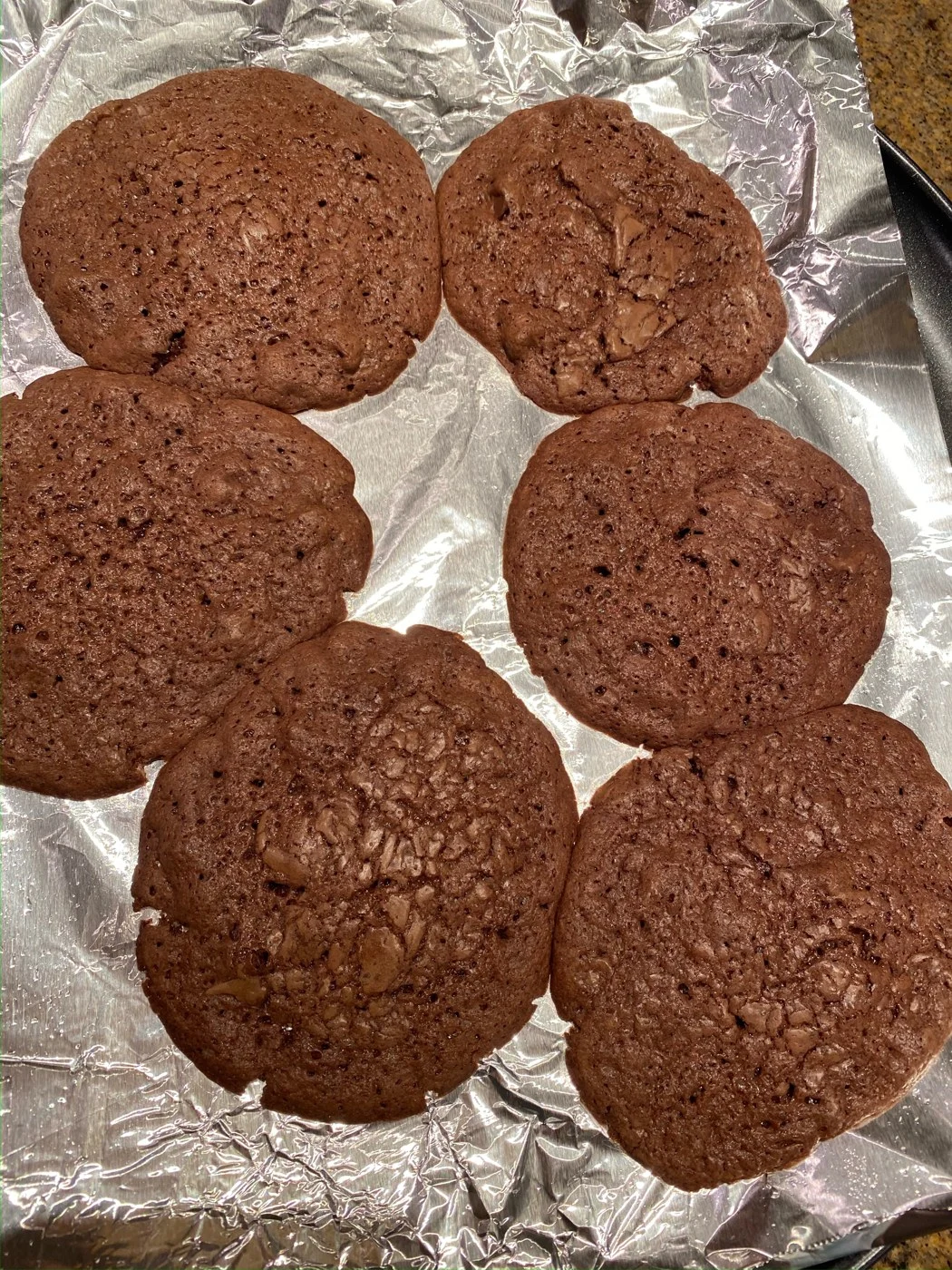 Six broad cocoa-colored cookies with crackled tops on foil.
