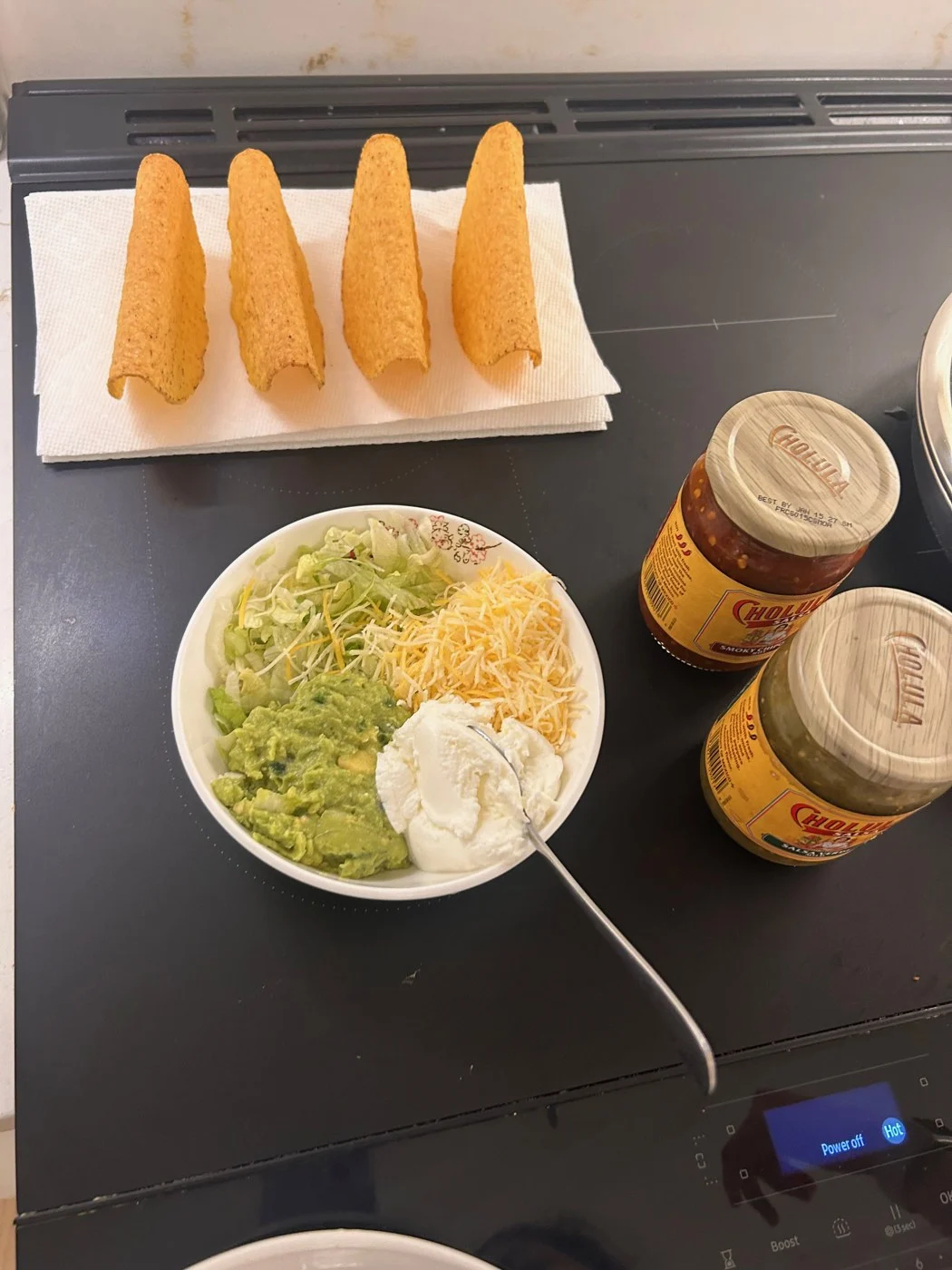 A closer view of empty taco shells, shredded toppings, a white condiment and sauce jars.