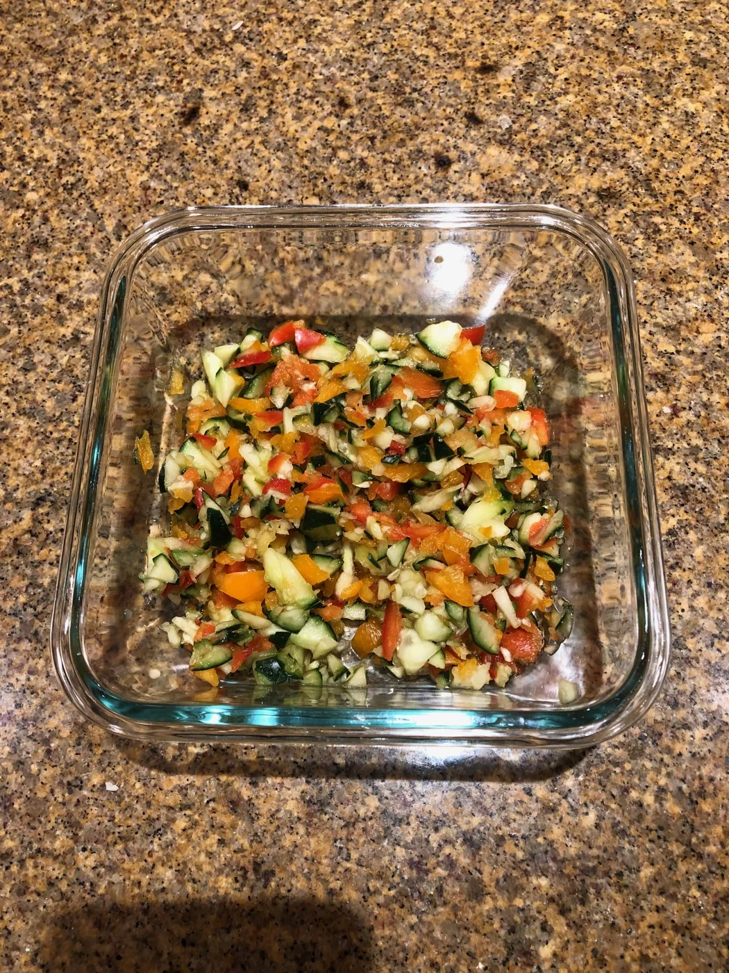 A colorful chopped vegetable mixture in a square glass dish.