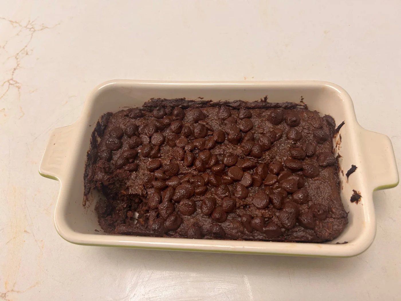 A dark chocolate-colored sheet cake topped with chocolate chips in a ceramic dish.