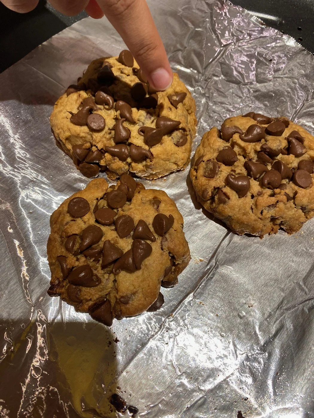 A finger pointing to one of three cookies loaded with chocolate chips.
