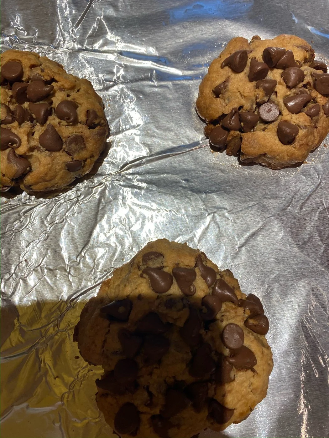 Three cookies topped with chocolate chips photographed close up on foil.