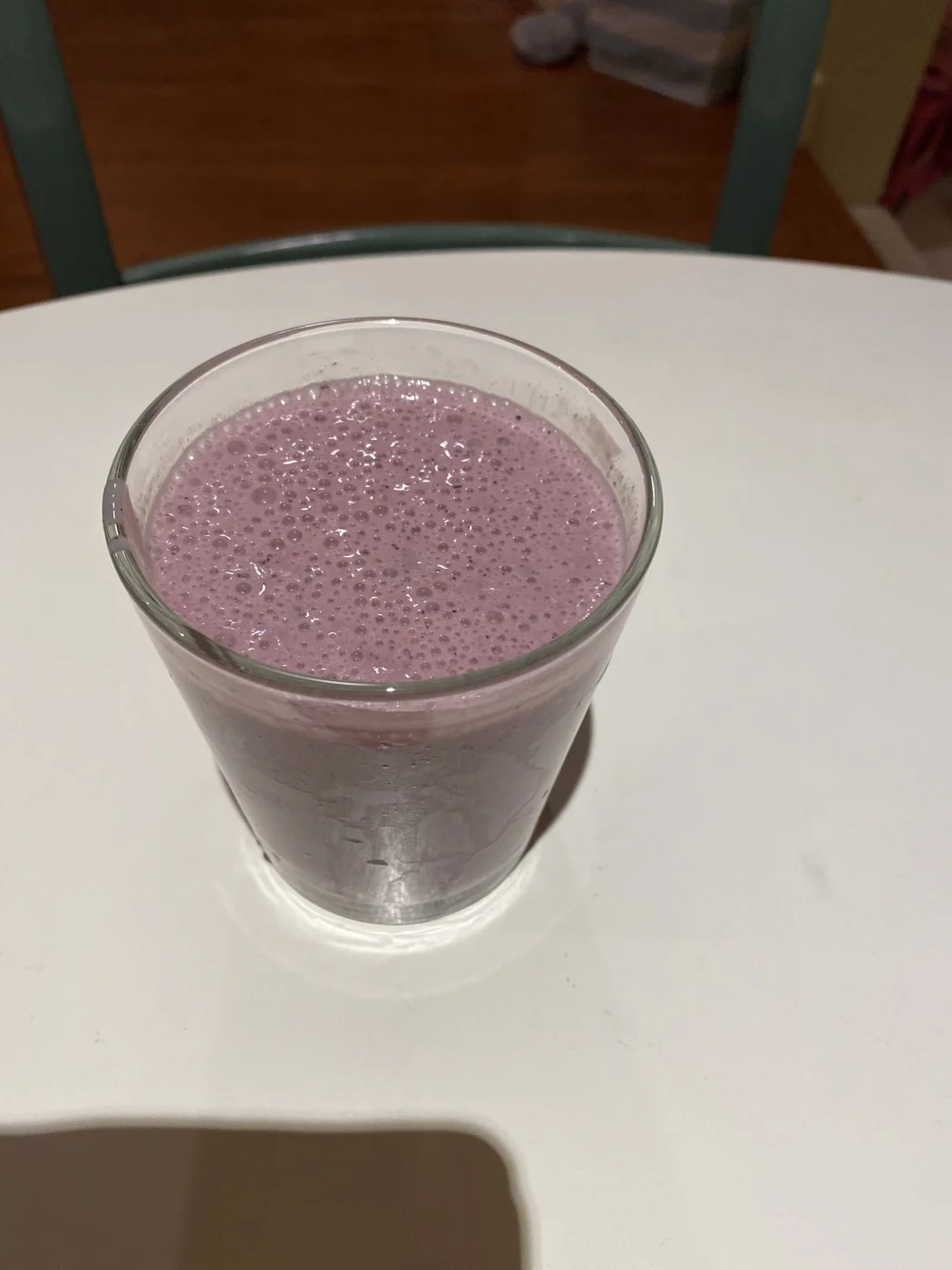 A glass of dark purple smoothie on a white tabletop.