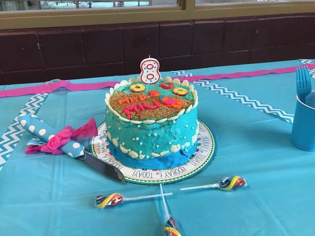 Turquoise frosted birthday cake with piped sea-themed decoration and number 8 candle.