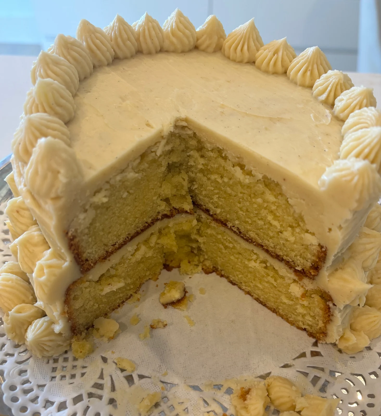 Two yellow cake layers, smooth pale exterior frosting, piped shell/dollop borders and a narrow brown center seam.