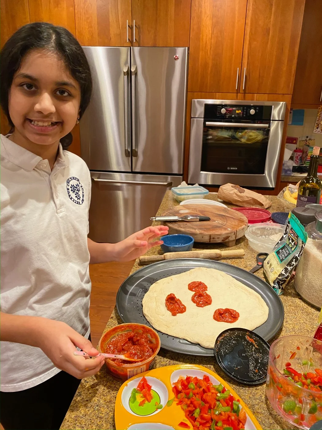 Adding tomato sauce to a round pizza base with chopped peppers nearby.