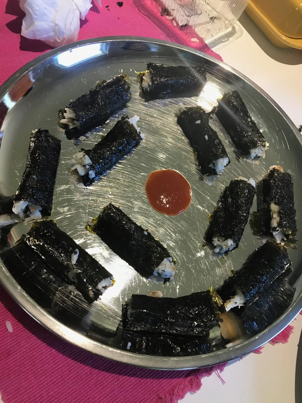 Seaweed-wrapped rice rolls arranged around a spot of red sauce on a steel plate.